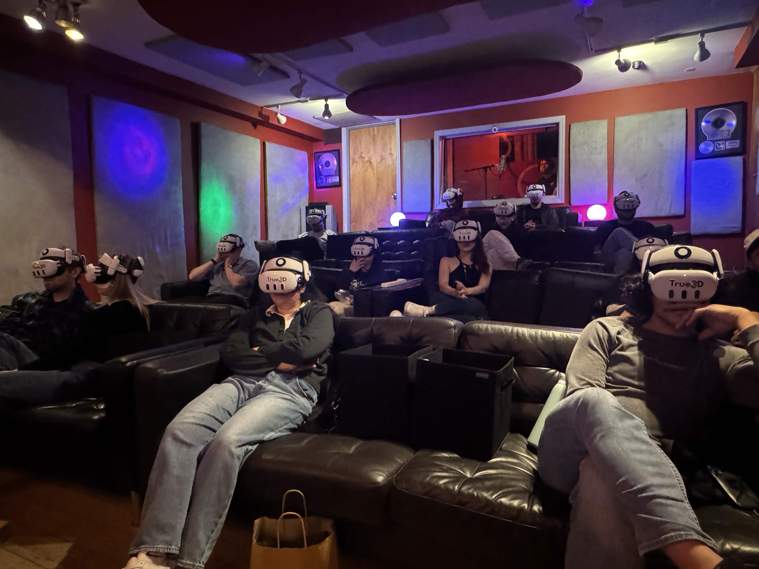 A screening room full of people on leather couches, all wearing True3D headsets, watching the same film together.
